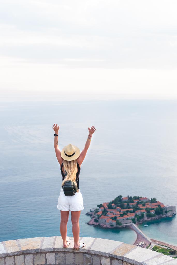 Powrót widzenia kobieta stojąc z podniósł ręce i patrząc na saint stephen wyspa na Adriatyku, Budva, Czarnogóra - Zdjęcie, obraz