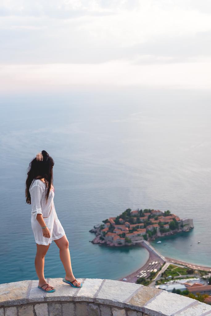 Zijaanzicht van de vrouw op zoek op het eiland van Sveti Stefan met hotel resort in de Adriatische Zee, Budva, Montenegro - Foto, afbeelding