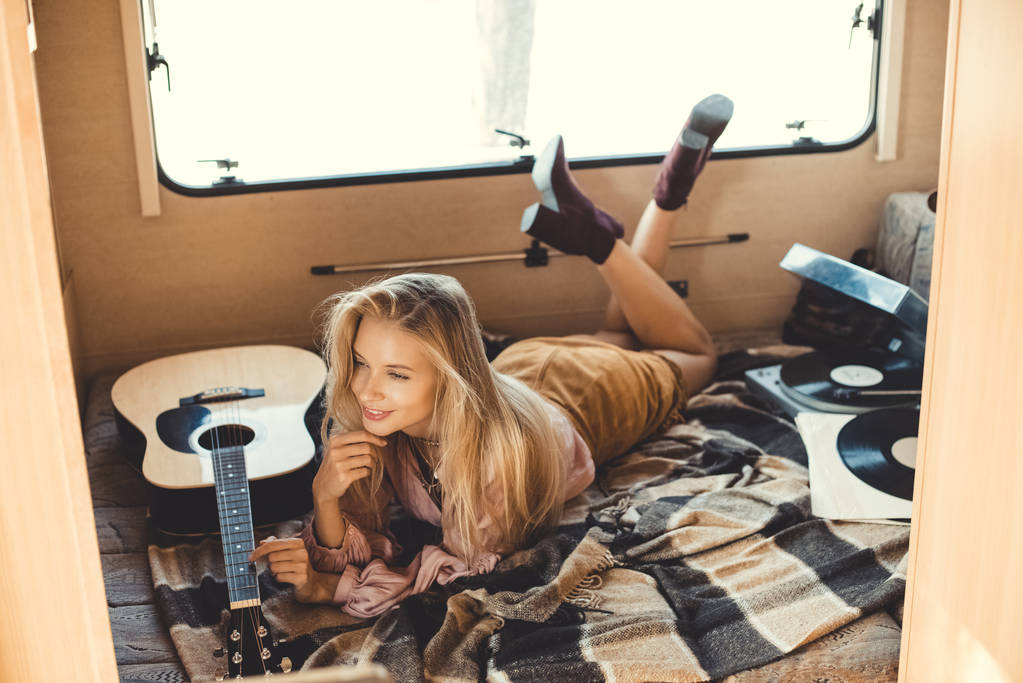 jonge vrouw liggen binnen camper met akoestische gitaar en vinyl speler  - Foto, afbeelding