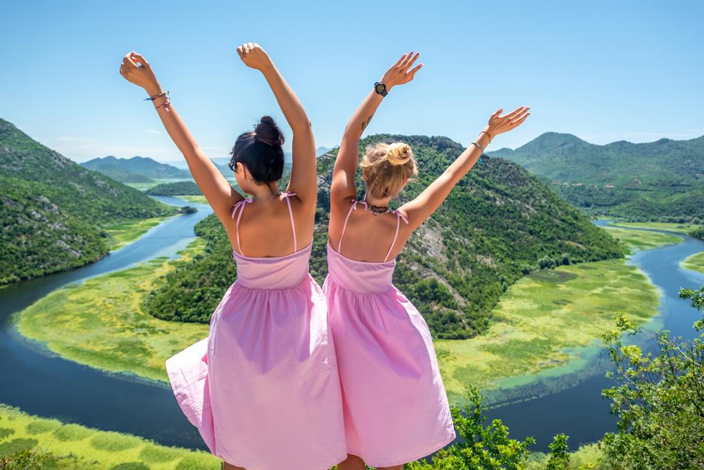 Arkadan görünüm kadınların Crnojevica Nehri (Rijeka Crnojevica) Karadağ'ın yakınında kaldırdı elleriyle duran Pembe elbiseler - Fotoğraf, Görsel