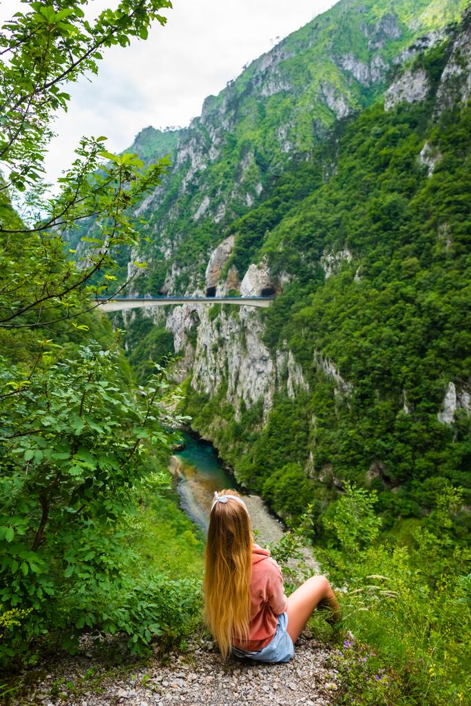 вид сзади женщины, смотрящей на мост между горами над рекой Пива в каньоне Пива в Монтенегро
 - Фото, изображение