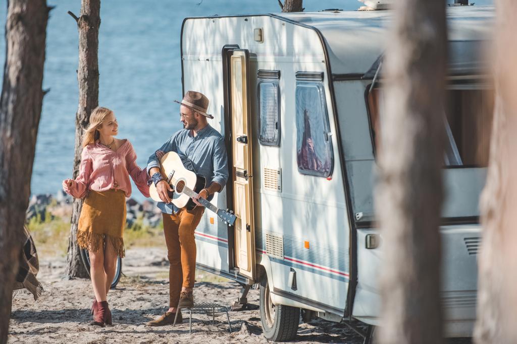 hippi tyttöystävä tanssii kun poikaystävä soittaa kitaraa lähellä traileri luonnossa
 - Valokuva, kuva