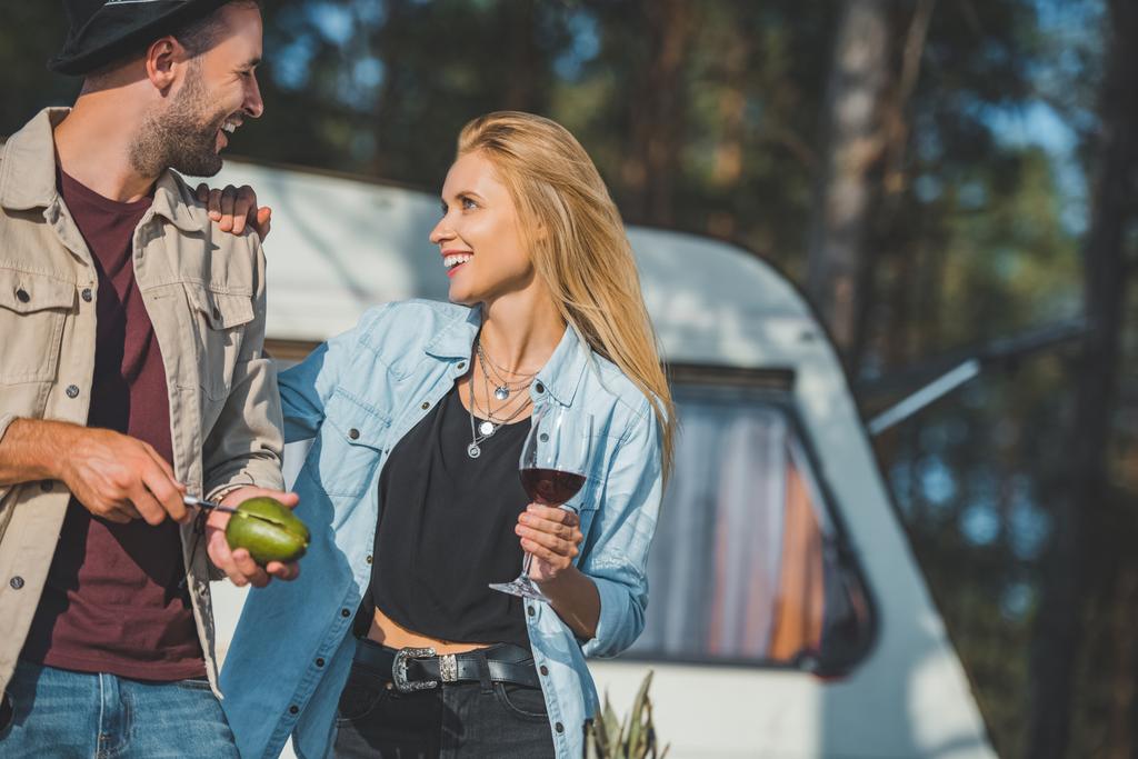 красивий усміхнений чоловік ріже авокадо, а дівчина з вином дивиться на нього
 - Фото, зображення
