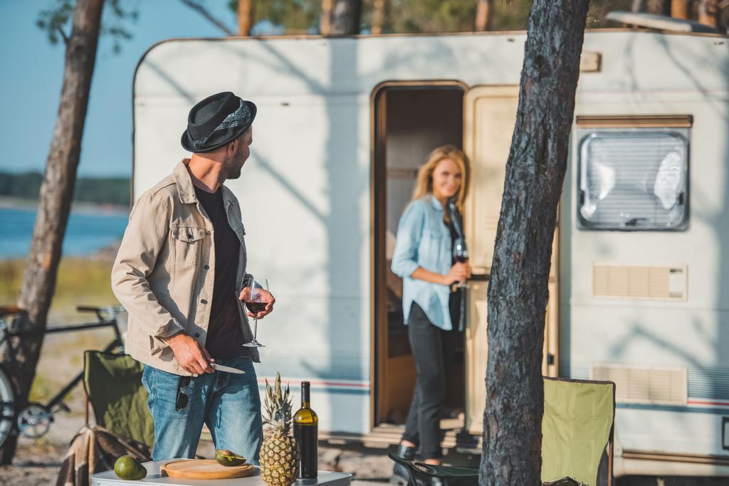 selective focus of handsome man with glass of wine looking at girlfriend near trailer - Photo, Image