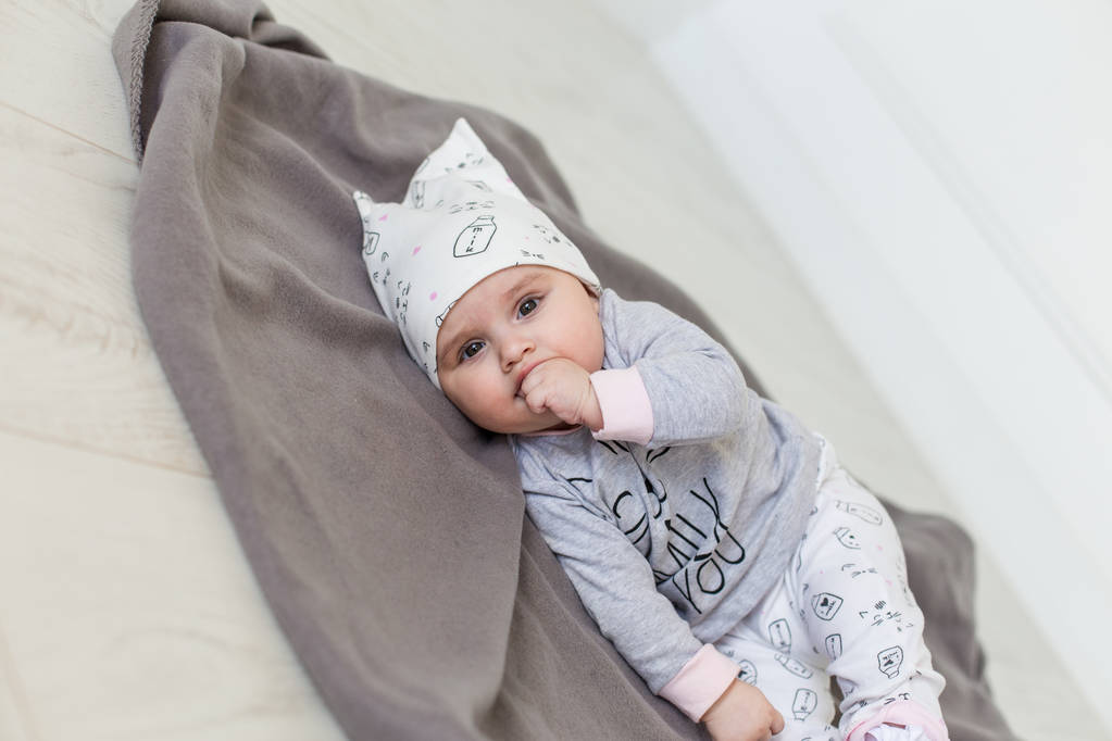 かわいい赤ちゃんが横になっている灰色の毛布と口の中に指を保持します。幸せな子供時代のコンセプト. - 写真・画像