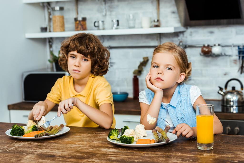 bambini annoiati mangiare verdure e guardando la fotocamera
 - Foto, immagini