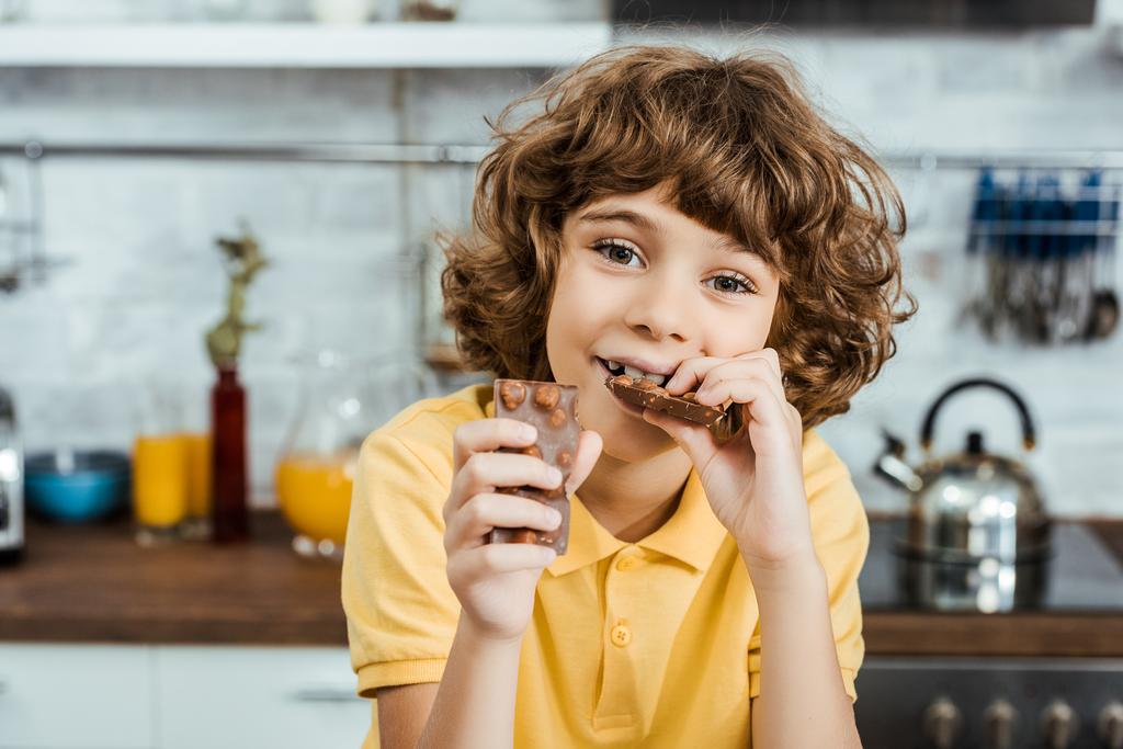 αξιολάτρευτο ευτυχισμένο αγόρι τρώει σοκολάτα με φουντούκια και βλέπουν τα φωτογραφικών μηχανών  - Φωτογραφία, εικόνα