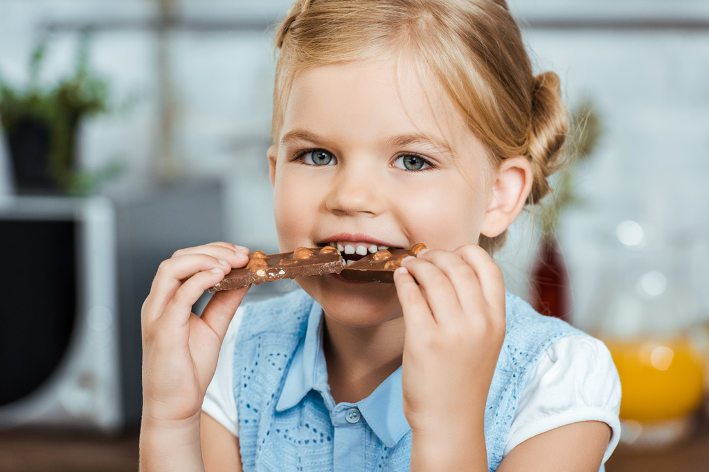 adorable niño comiendo delicioso chocolate y sonriendo a la cámara
  - Foto, imagen