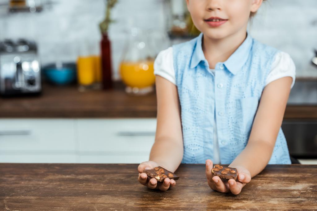 Schnappschuss eines lächelnden Kindes mit süßen Schokoladenstücken mit Haselnüssen - Foto, Bild