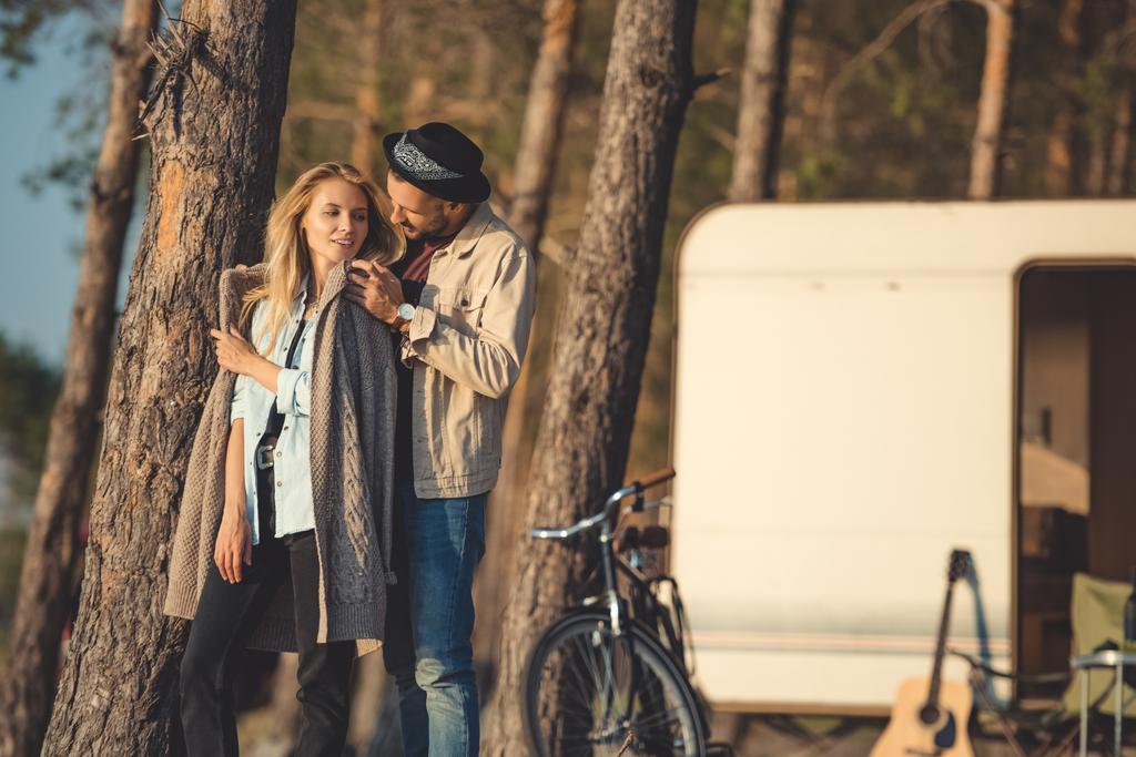 beautiful young couple hugging near trailer in forest - Photo, Image