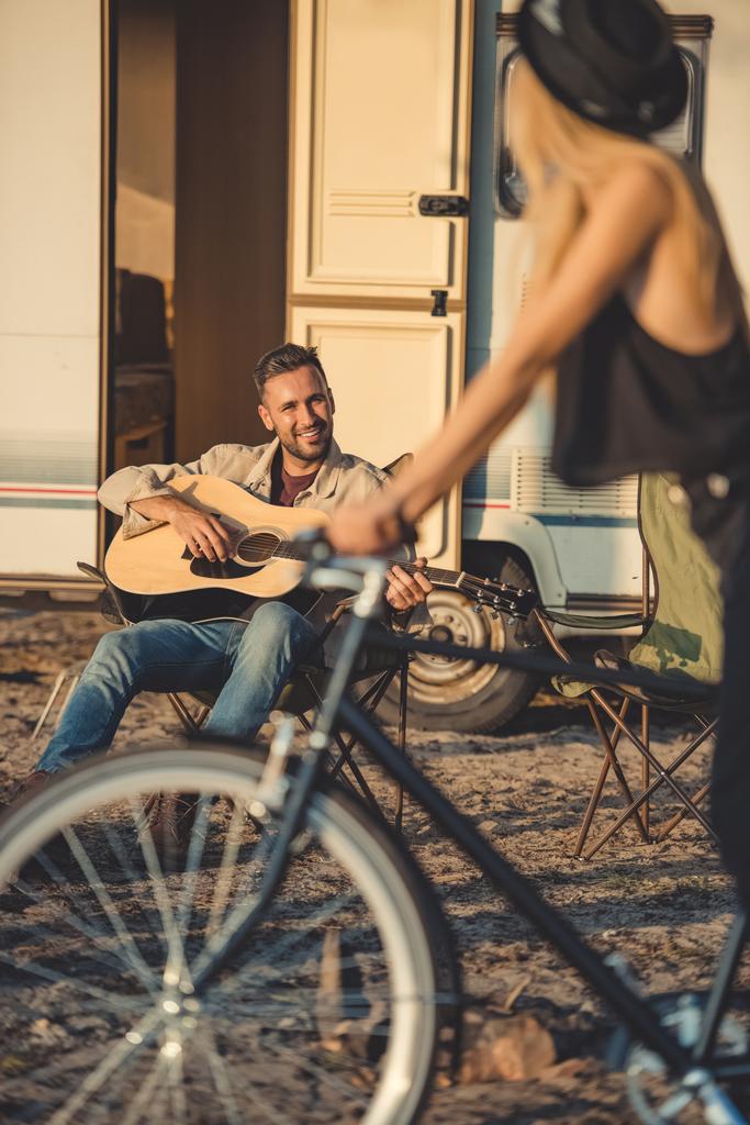 messa a fuoco selettiva di ragazza con bicicletta e uomo suonare la chitarra vicino rimorchio
 - Foto, immagini