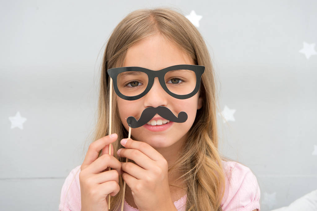 Girl pose with photo booth props glasses and mustick in bedroom. Κορίτσι με γυαλιά για πάρτι. Το παιδί μιμείται τον ανδρισμό ή θέλει να μοιάζει με τον πατέρα της. Παιδί με μουστάκι και γυαλιά - Φωτογραφία, εικόνα
