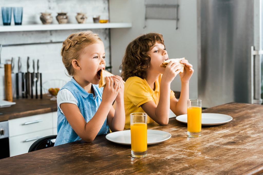 schöne Kinder sitzen am Tisch und essen leckere Sandwiches - Foto, Bild
