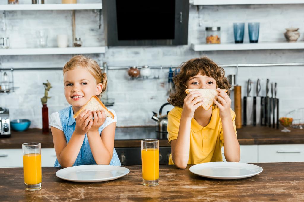 очаровательные счастливые дети едят вкусные бутерброды и улыбаются в камеру
 - Фото, изображение
