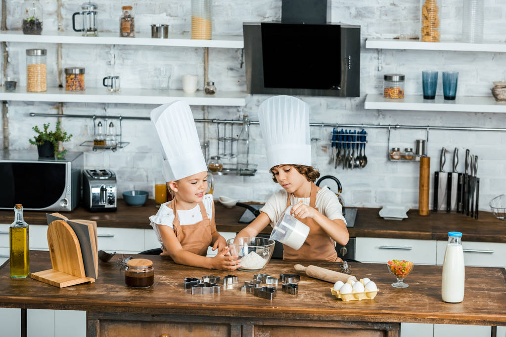 αξιολάτρευτο μικρό παιδιά σε καπέλα σεφ προετοιμάζει ζύμη για μπισκότα στην κουζίνα  - Φωτογραφία, εικόνα