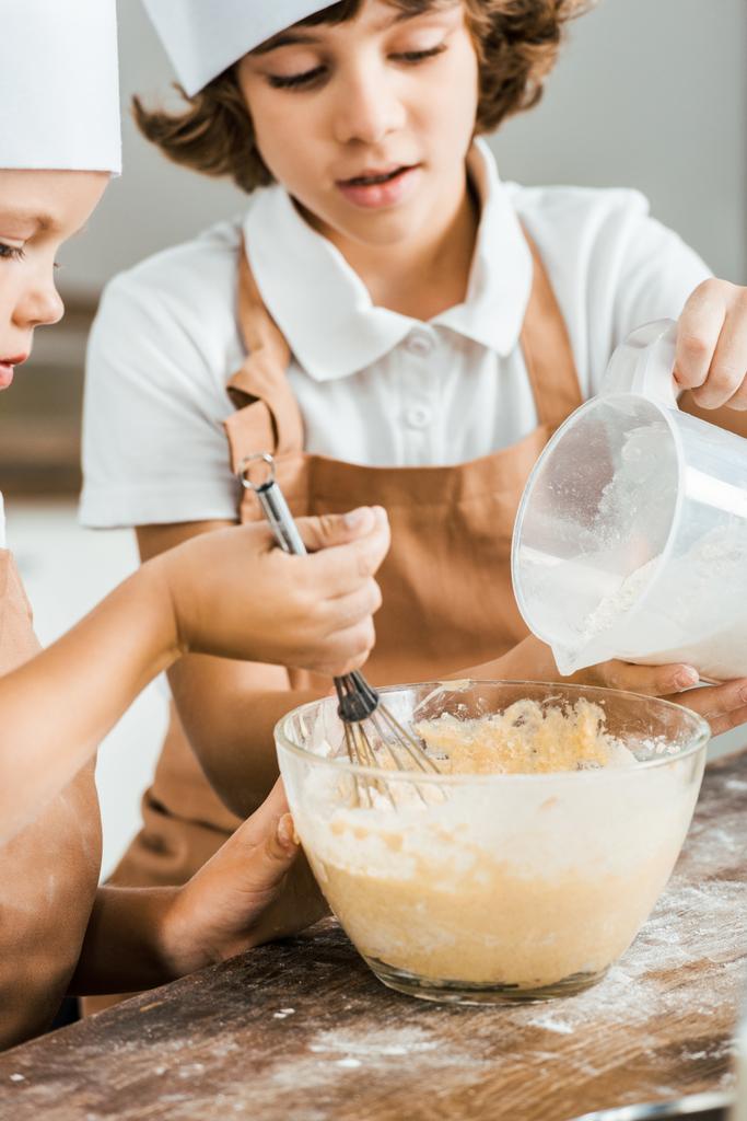 tiro cortado de crianças em aventais e chapéus de chef preparando a massa de farinha para biscoitos saborosos em conjunto
   - Foto, Imagem