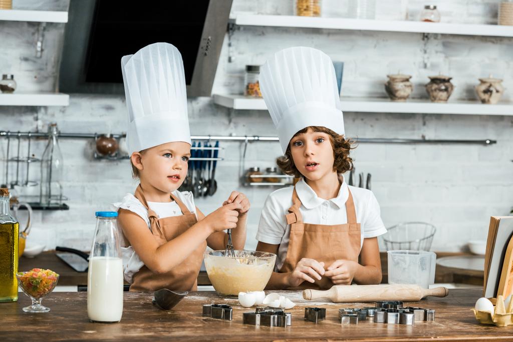 очаровательные дети в фартуках и шляпах шеф-повара готовят тесто для вкусного печенья вместе
  - Фото, изображение
