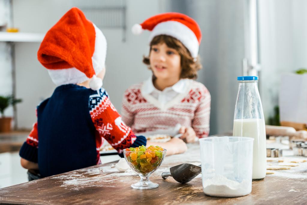 adorable kids in santa hats looking at each other while cooking together - Photo, Image