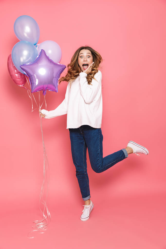 Volledige lengte portret van een verbaasd jonge vrouw stelletje lucht ballonnen houden terwijl springen geïsoleerd op roze achtergrond - Foto, afbeelding