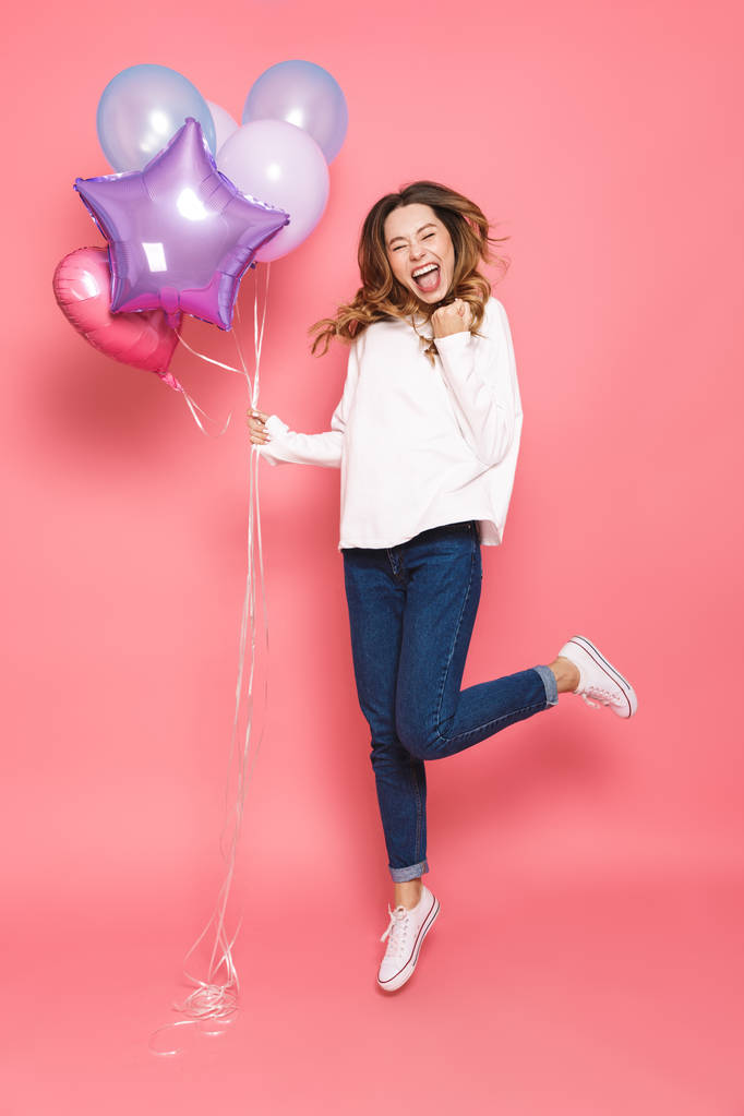 Ολόσωμο πορτρέτο του ένα ενθουσιασμένος νεαρή γυναίκα κρατώντας μάτσο μπαλόνια αέρα ενώ άλματα απομονώνονται σε ροζ φόντο - Φωτογραφία, εικόνα