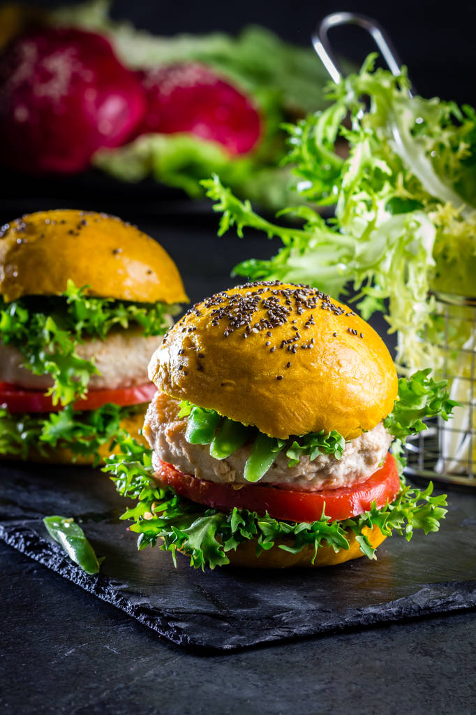 Gelbe Burger. hausgemachte amerikanische Chicken Burger Hamburger mit Kurkuma und Chia-Brötchen und Gemüse. trendiges Essen. Nahaufnahme, Schieferhintergrund. - Foto, Bild