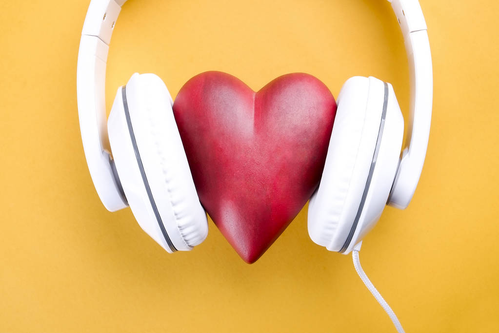 Senin kalp kavramı dinle. Parlak sarı zemin üzerinde beyaz kulaklık ile büyük kırmızı kalp. Sevgililer günü kompozisyon kulaklık ve kalp. Yakın çekim, kopya alanı, üstten görünüm, düz lay, - Fotoğraf, Görsel