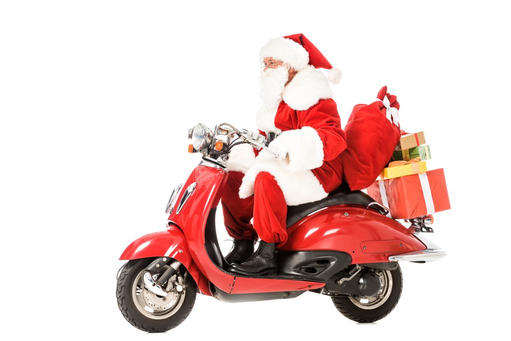 вид збоку Санта-Клауса, що верхи на старовинному червоному скутері з мішками та подарунковими коробками ізольовані на білому
 - Фото, зображення