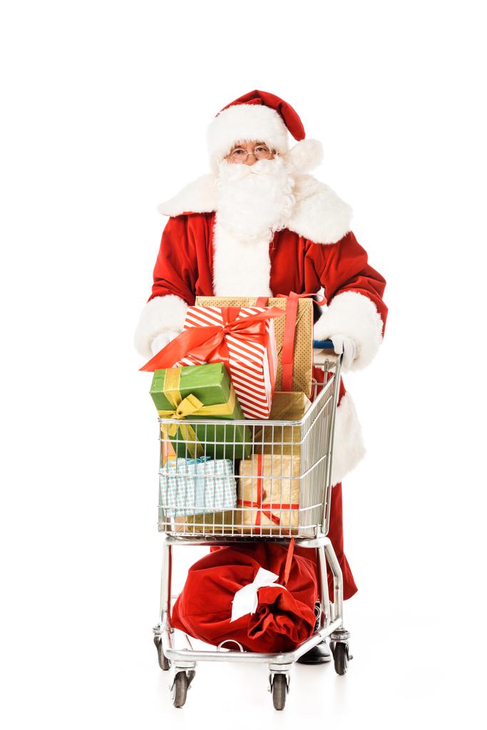 Weihnachtsmann mit Einkaufswagen voller Geschenkboxen, die in die Kamera schauen, isoliert auf weiß - Foto, Bild