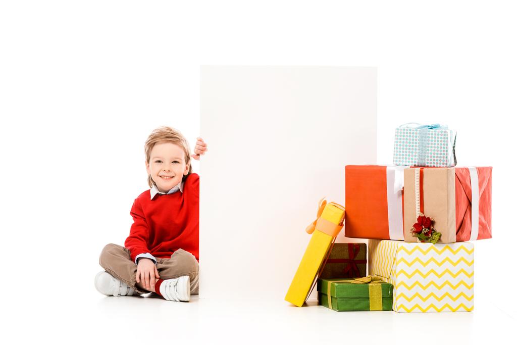 glückliches kleines Kind mit Stapel Weihnachtsgeschenke und leere Bretter isoliert auf weiß - Foto, Bild