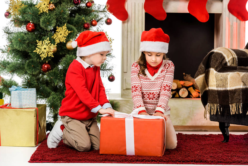 weinig kinderen openen rode kerstcadeau zittend op de vloer - Foto, afbeelding