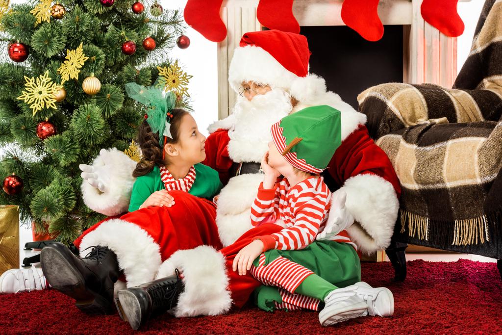 Père Noël embrassant les enfants alors qu'ils sont assis sur le sol devant la cheminée ensemble
 - Photo, image