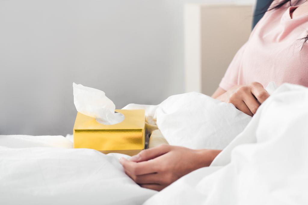 abgeschnittene Aufnahme einer kranken Frau mit einer Schachtel Papierservietten im Bett - Foto, Bild