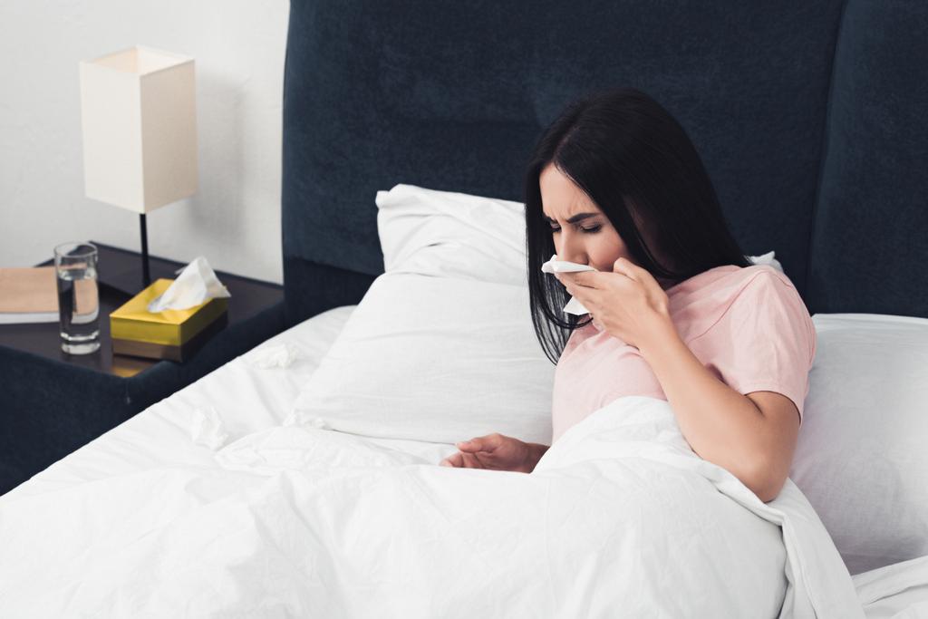 больная молодая женщина с кашлем лежит в постели с салфетками
 - Фото, изображение