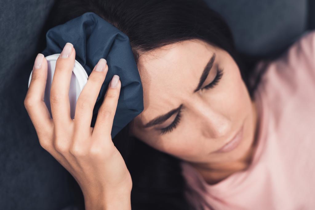 primo piano di una giovane donna malata che tiene il ghiaccio sulla testa mentre è sdraiata a letto
 - Foto, immagini