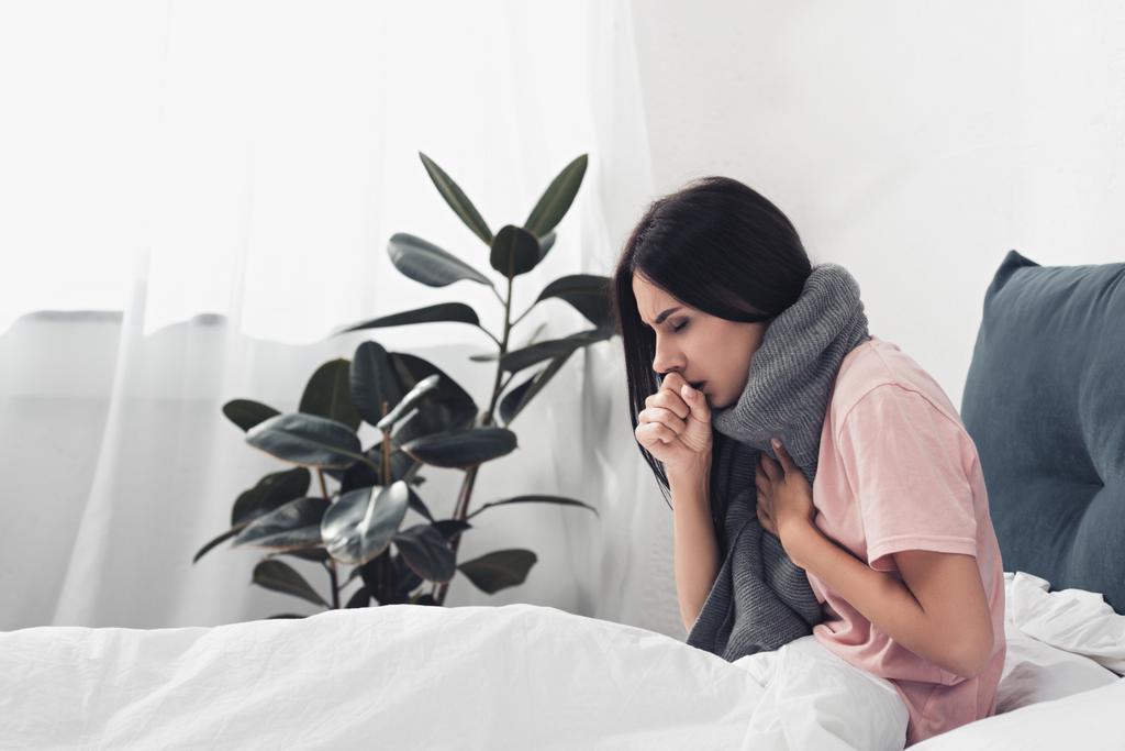 nemocný mladá žena seděla v posteli a má kašel, zatímco trpí bolest v krku - Fotografie, Obrázek