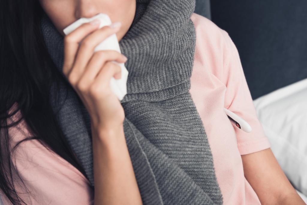 ベッドで咳嗽時ナプキンで口を覆っている病気の若い女性のクロップ撮影 - 写真・画像