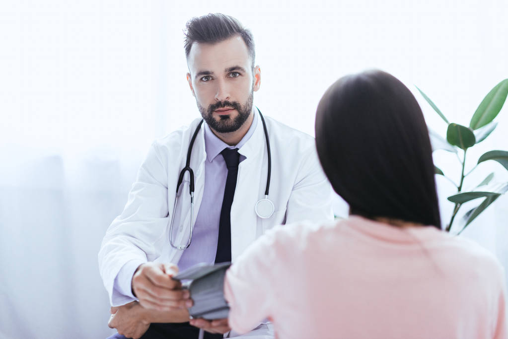 handsome young doctor listening to female patient and looking at camera - Photo, Image