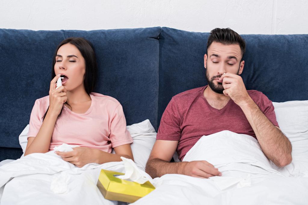 sick couple using cough and nose spray while sitting in bed - Photo, Image