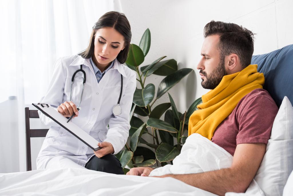 female doctor showing clipboard with documents to patient while lying in bed - Photo, Image