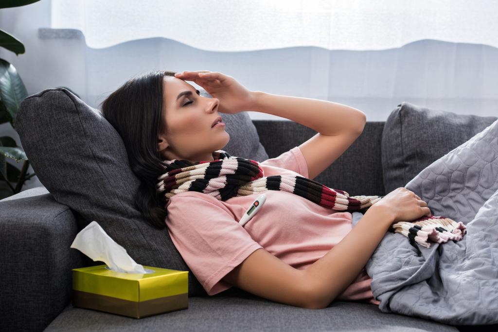 mujer joven enferma que mide la temperatura con termómetro eléctrico en el sofá
 - Foto, Imagen