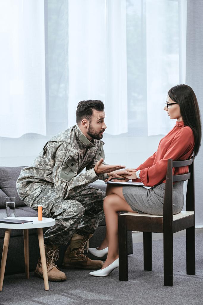 сердитий солдат розмовляє у психіатра і жестикулює під час сеансу терапії
 - Фото, зображення