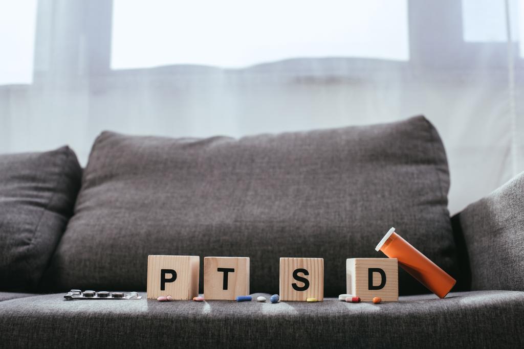cubos de madera con signos de trastorno de estrés postraumático abreviatura (PTSD) acostado en el sofá con varias pastillas
 - Foto, Imagen