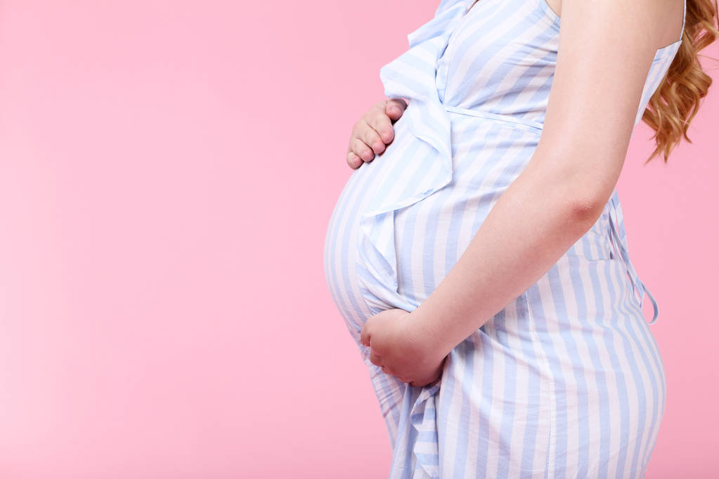 ピンクの背景の縞模様のドレスに妊娠中の女性 - 写真・画像
