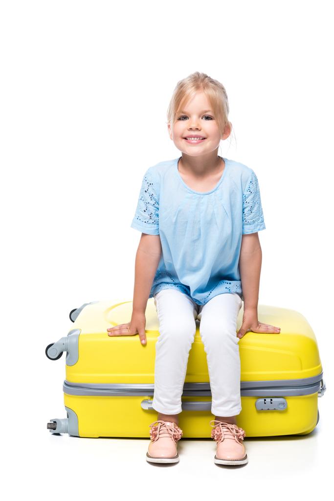 Kind sitzt auf gelbem Gepäck isoliert auf weißem - Foto, Bild