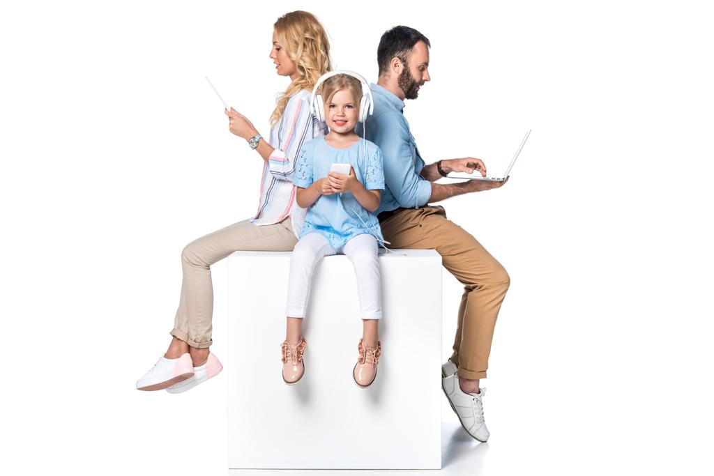 família usando dispositivos digitais e sentado em cubo branco isolado em branco
 - Foto, Imagem