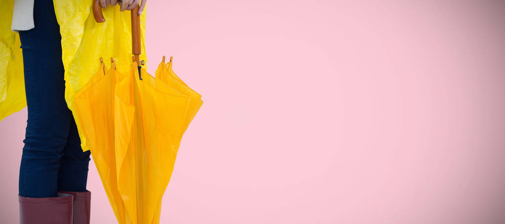 ピンクの背景に傘を保持している黄色のレインコートの女 - 写真・画像