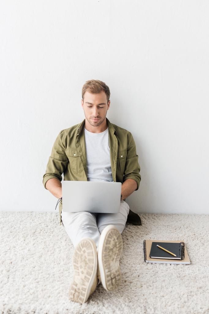 casual man using laptop on beige rug, remote work - Photo, Image