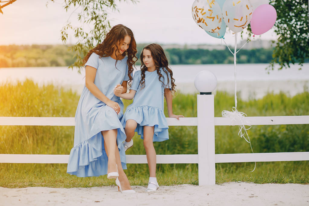 Mom and daughter in identical dresses are sitting in a park  - Photo, Image