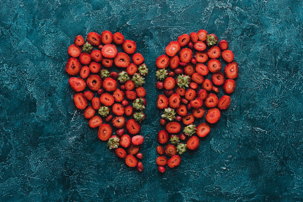 vue de dessus du signe de coeur coupé en deux en fraises sur la surface en béton bleu
 - Photo, image