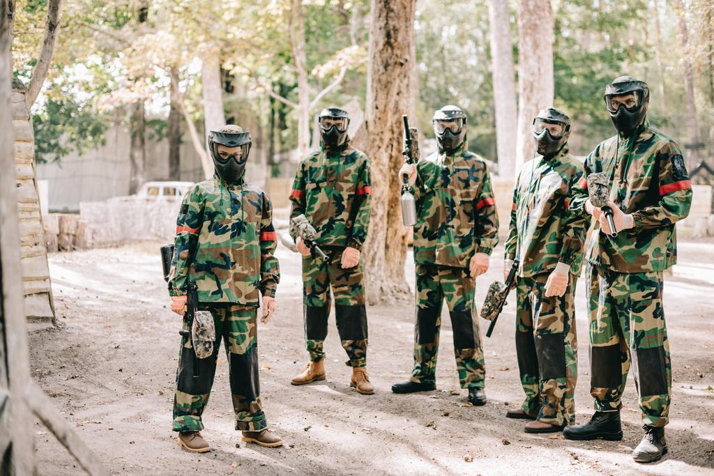 пейнтбольная команда в форме и защитных масках стоит на улице с пейнтбольными пушками
 - Фото, изображение